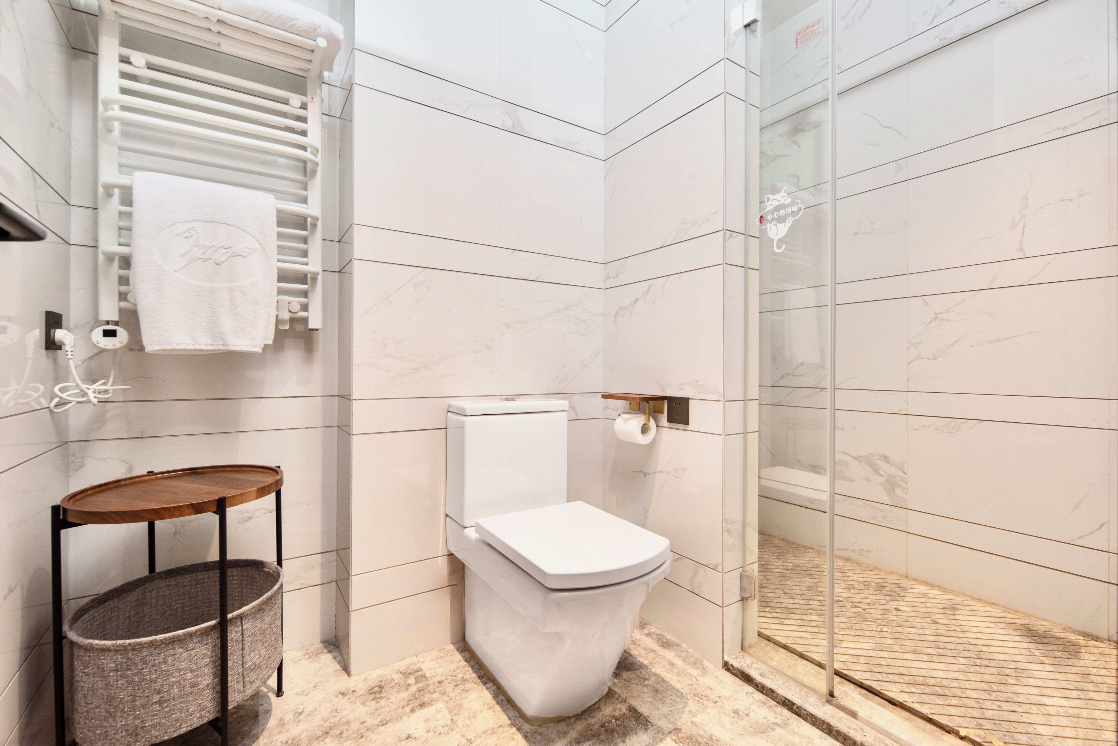 A modern bathroom with a toilet, a towel rack, a small wooden table, and a basket.