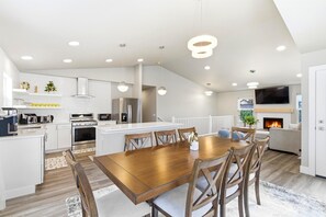 A modern kitchen with white cabinetry, stainless steel appliances, and a dining area with a wooden table and chairs. - LE11: 4-bedroom 3full bathroom house in gorgeous Anchorage neighborhood (Anchorage)