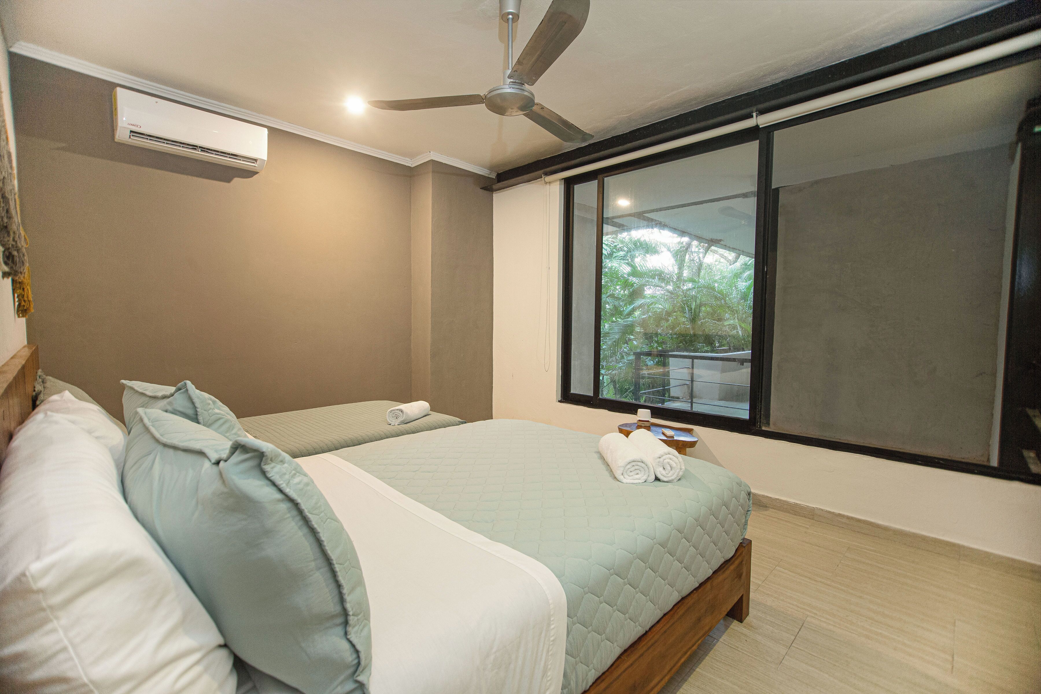 A bedroom with two beds, a ceiling fan, an air conditioner, and a large window.