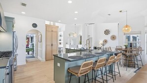 A modern kitchen with a central island, bar stools, and a dining area with a high ceiling and pendant lighting. - Pearl of Paradise | Waterfront Pool Home w/ Dock in Palm Coast, Game Room, Near Flagler Beach (Palm Coast)