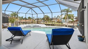 A covered outdoor swimming pool with two lounge chairs, a view of a residential neighborhood, and a clear sky. - Pearl of Paradise | Waterfront Pool Home w/ Dock in Palm Coast, Game Room, Near Flagler Beach (Palm Coast)