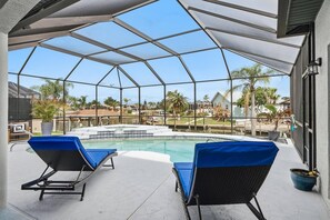 A covered outdoor swimming pool with two lounge chairs, a view of a residential neighborhood, and a clear sky. - Pearl of Paradise | Waterfront Pool Home w/ Dock in Palm Coast, Game Room, Near Flagler Beach (Palm Coast)
