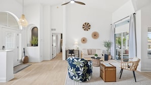 Un vaste espace de vie doté d’une grande fenêtre, d’un ventilateur de plafond et d’un coin salon avec un canapé et des fauteuils.