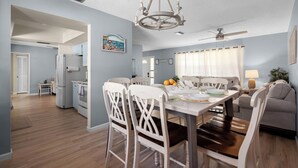 A dining area with a table set for four, white chairs, a chandelier, and a ceiling fan. - AMI Escape in 10 Min! Pool, Spa, Firepit & Game Room – Pet Friendly (Bradenton)