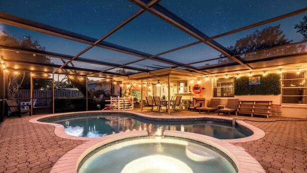 A covered outdoor swimming pool area with a hot tub, lounge chairs, and string lights. - AMI Escape in 10 Min! Pool, Spa, Firepit & Game Room – Pet Friendly (Bradenton)