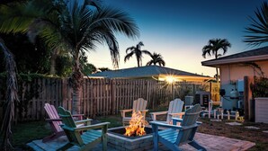 A backyard with a fire pit surrounded by Adirondack chairs, a wooden fence, and palm trees. - AMI Escape in 10 Min! Pool, Spa, Firepit & Game Room – Pet Friendly (Bradenton)