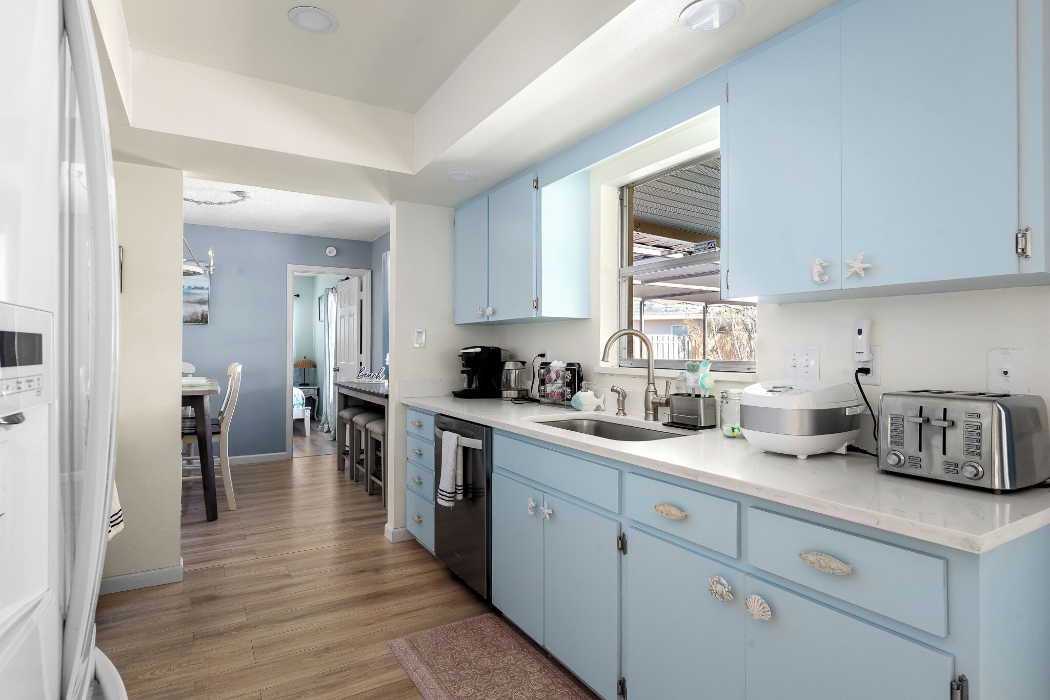 A modern kitchen with light blue cabinets, stainless steel appliances, and a large window.