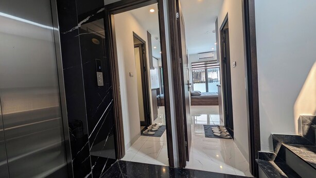 A modern hallway with a marble floor, a door with a number plate, and a view into a room with a bed and a window. - Aira Khuong Thuong Apartment (Hanoi)