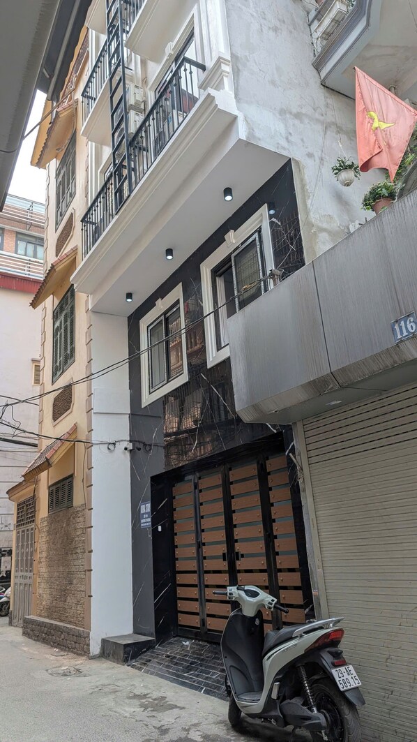 A multi-story residential building with a gated entrance, a parked scooter, and a visible sign indicating a parking area. - Aira Khuong Thuong Apartment (Hanoi)