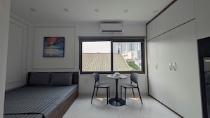 A compact bedroom with a bed, a small table with chairs, a window with a view of buildings, and a wardrobe. - Aira Khuong Thuong Apartment (Hanoi)