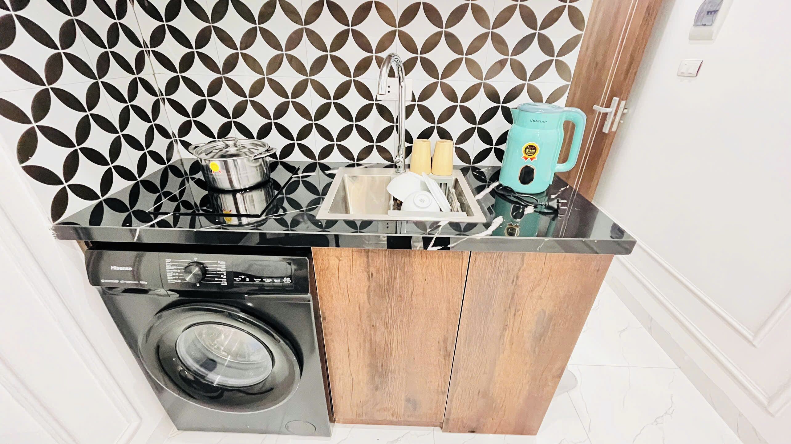 Une cuisine compacte équipée d’un lave-linge, d’un évier et d’une machine à café.