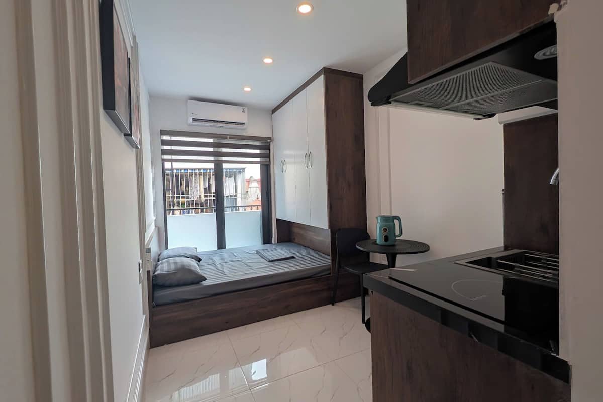 A compact kitchen with a built-in stove, a small table with a kettle, and a view of the outside balcony.