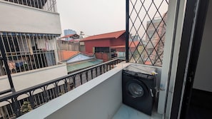 Een balkon met een wasmachine, een metalen hekwerk en uitzicht op omliggende gebouwen.
