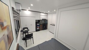 Een compacte hotelkamer met een kitchenette, een wasmachine, een eettafeltje en een stoel.