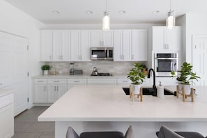 A modern kitchen with white cabinets, a central island, stainless steel appliances, and pendant lighting.