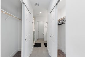 A narrow hallway with white walls, a wooden closet rod, a white door, and a black doormat.