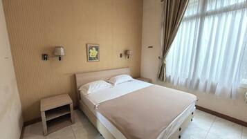 A hotel room with a bed, bedside tables, wall-mounted lamps, a window with curtains, and a framed picture on the wall.