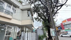 A building with a gated entrance, a visible signboard, and a tree in front. - Guesthouse Anggrek BSD (South Tangerang)