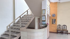 A reception area with a curved counter, a staircase, and framed certificates on the wall. - Guesthouse Anggrek BSD (South Tangerang)
