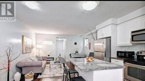 A modern kitchen with white cabinets, stainless steel appliances, and a marble island. - 1 bed 1 bath Townhome (Kitchener)
