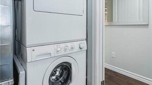 A stacked washer and dryer unit in a room with a white door and a mirror above it. - 1 bed 1 bath Townhome (Kitchener)