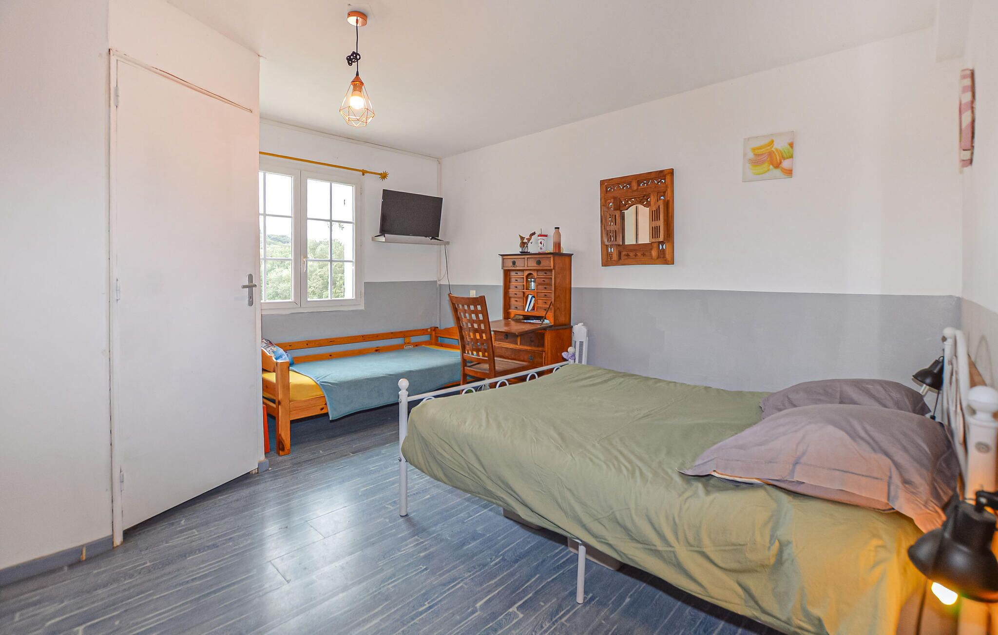 A bedroom with a bed, a desk, a chair, a TV, and a window.