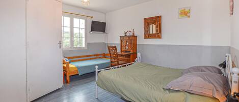 A bedroom with a bed, a desk, a chair, a TV, and a window.