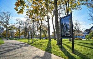 Un parc avec un chemin pavé, des arbres aux feuilles jaunes et une affiche sur un poteau.