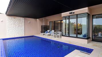 Ein Swimmingpool mit blauen Fliesen, weißen Liegestühlen und einer Steinmauer.