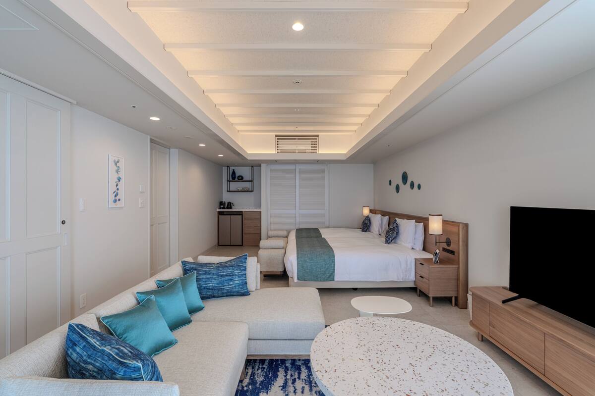 Une chambre d’hôtel moderne équipée d’un lit, d’un canapé, d’une télévision et d’une petite kitchenette.