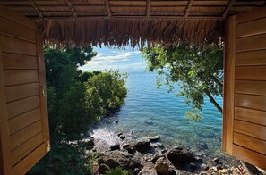 A wooden room with a view of a clear blue lake, surrounded by greenery.
