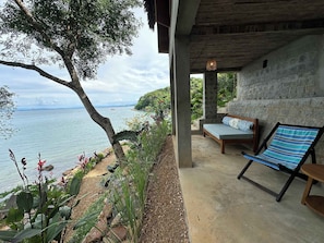 A covered outdoor seating area with a view of the sea, a stone wall, and a wooden bench.