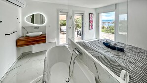 Een moderne badkamer met een badkuip, een wastafel met spiegel en uitzicht op het omliggende landschap.