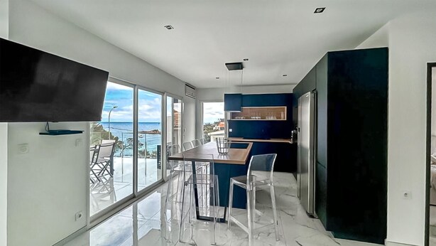 Een moderne keuken met een groot schiereiland, een eetgedeelte met transparante stoelen en uitzicht op de oceaan.
