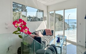 A modern living room with a glass coffee table, a sofa with cushions, a vase with flowers, and a view of the sea through large windows. - 3 bedroom beautiful home in Roquebrune-sur-Argens (Roquebrune-sur-Argens)