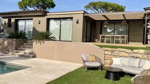Ein modernes Haus mit Swimmingpool, Sitzgelegenheiten im Freien und einer Steinmauer.