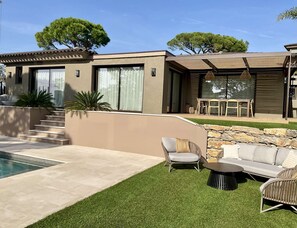 Ein modernes Haus mit Swimmingpool, Sitzgelegenheiten im Freien und einer Steinmauer.