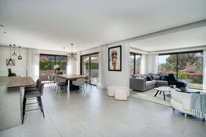 A modern living room with a dining area, large windows, and a view of greenery. - VILLA WITH POOL NEAR THE TOWN CENTER FOR RENT FOR 8 PEOPLE (STE MAXIME)