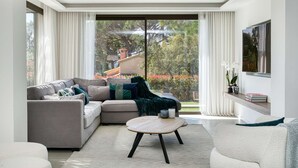Ein modernes Wohnzimmer mit einer Couch, einem Couchtisch und einem großen Fenster mit Vorhängen.