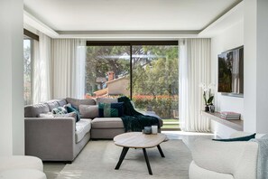 Ein modernes Wohnzimmer mit einer Couch, einem Couchtisch und einem großen Fenster mit Vorhängen.
