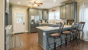 Una cocina con una isla central, taburetes de bar, un refrigerador y un ventilador de techo.