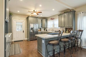 A kitchen with a central island, bar stools, a refrigerator, and a ceiling fan.