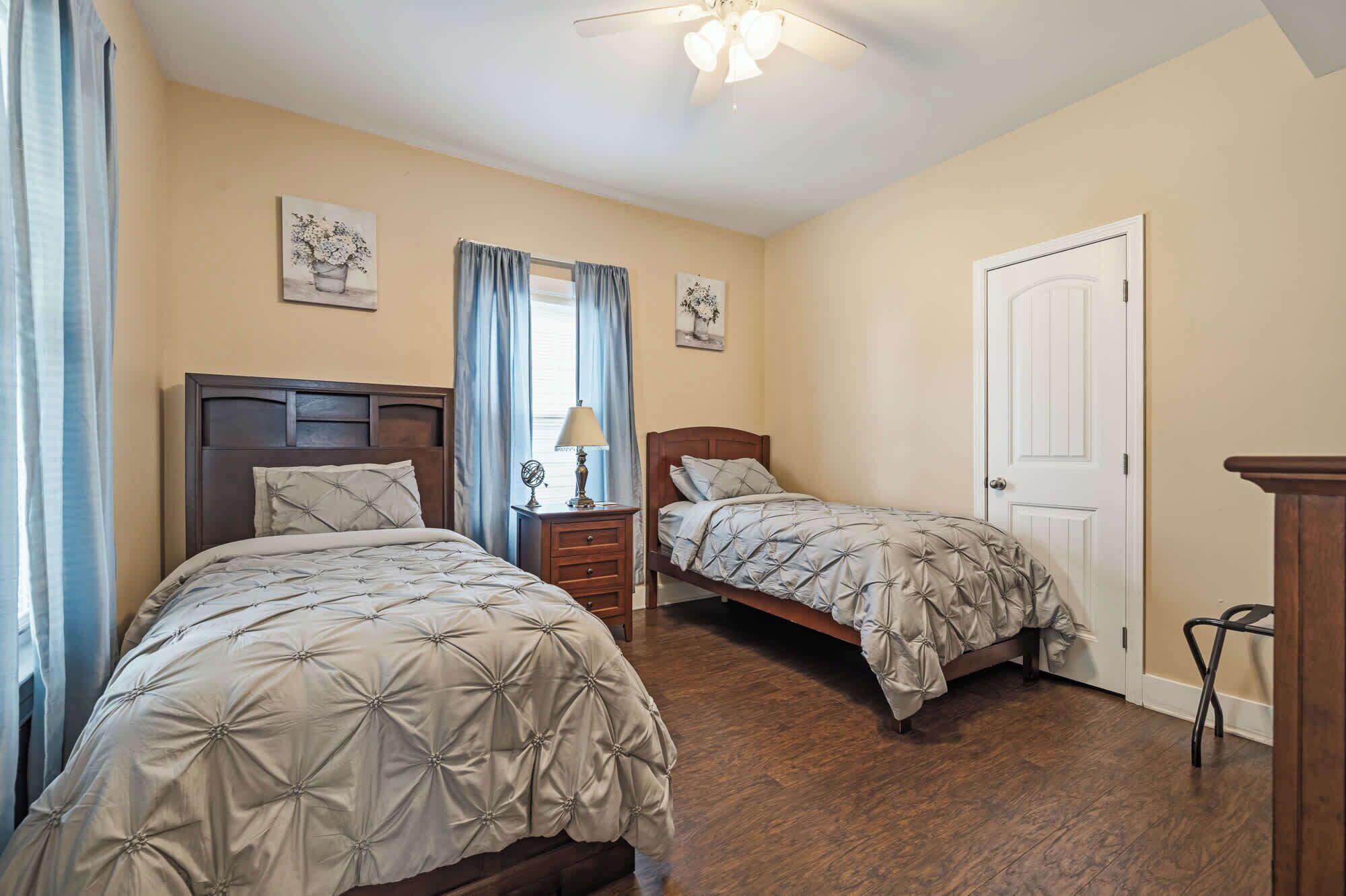 A bedroom with two beds, a nightstand, a lamp, and a door.