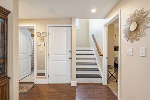 A hallway with a wooden floor, a white door, a staircase with black steps, and a wall-mounted mirror.