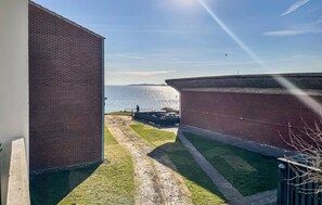 Blick auf ein Backsteingebäude mit einer Grünfläche und einem Gewässer im Hintergrund.