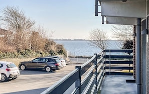 Ein Balkon mit Blick auf das Wasser, ein Parkplatz mit Autos und eine weiße Einfriedung.