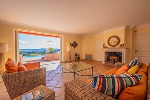 Ein Wohnzimmer mit Glastisch, Korbmöbeln, Kamin und Blick ins Freie.
