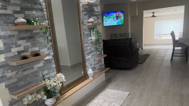 Ein modernes Wohnzimmer mit Steinwand, einem großen Spiegel, einem Flachbildfernseher, einer Couch und einem Essbereich mit Tisch und Stühlen.