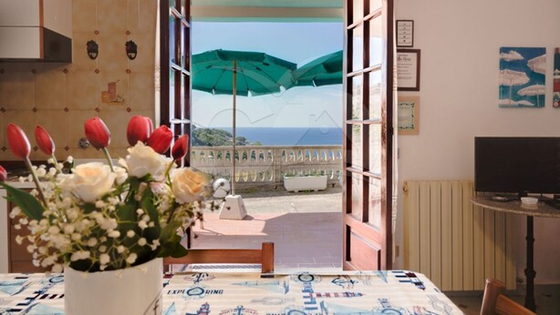 Una habitación con vista al mar, una mesa con un arreglo floral y un televisor sobre un mueble.