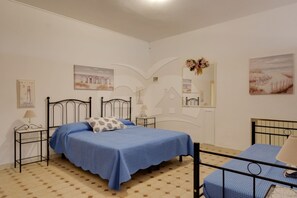 A bedroom with a bed, a smaller bed, a nightstand, a lamp, and wall art. - VILLA FLORA - Villa Flora - Mono 3 (Capoliveri)